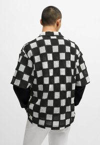 Lyhythihainen paita, jossa on mustavalkoinen ruutukuosi, valmistettu teksturoidusta kankaasta, jossa on rento istuvuus ja avonainen kaulus.