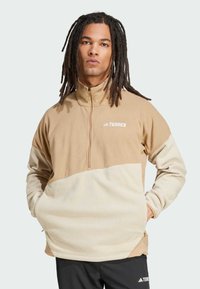 Beżowy i kremowy polarowy sweter z wysokim kołnierzem, zamkiem błyskawicznym oraz przednimi kieszeniami. Na klatce piersiowej znajduje się biały napis "TERREX".