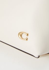 White leather handbag featuring a gold-tone logo accent, smooth texture, and black trim along the edges.