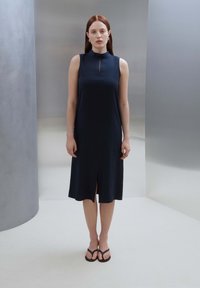 Navyblaues ärmelloses Kleid mit hochgeschlossenem Kragen, kleinem Schlitzdetails vorne und lockerer Passform. Glatte Stoffoberfläche vor einem neutralen Hintergrund.