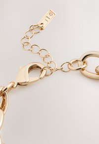 Gold chain clasp featuring interlocking links, a lobster claw closure, and a tag with a small gemstone accent. Smooth finish with reflective shine.