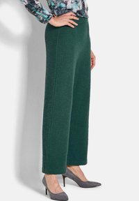Breedbenige groene gebreide broek met een gestructureerde afwerking, met een hoge taille en strakke lijnen, gecombineerd met grijze hoge hakken.