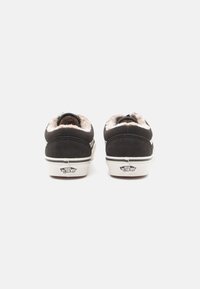 Pantofi slip-on negri din suede, cu o căptușeală din blană maro deschis și tălpi din cauciuc alb, având un logo pe călcâi și dungi negre de-a lungul tălpii.