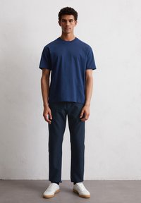 Navyblauwe crew neck t-shirt van katoen, gecombineerd met donkere broek en witte sneakers. Eenvoudig ontwerp, korte mouwen, effen kleur zonder patronen.