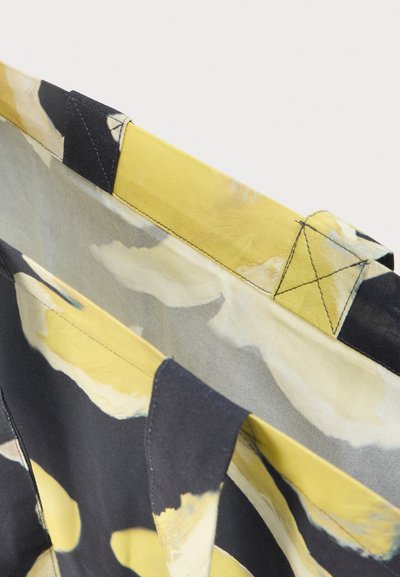 Mitmevärviline kott lillemustriga. Valmistatud kangast, kollastes ja mustades toonides, kontrastse õmblusega ja tugevate sangadega.