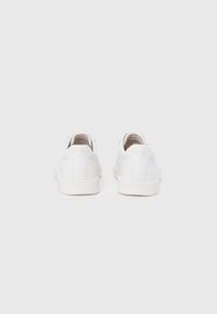 Άσπρα αθλητικά παπούτσια με λείο δέρμα στο πάνω μέρος, μινιμαλιστικό σχέδιο, επίπεδη σόλα και διακριτικό λογότυπο στη φτέρνα, χωρίς ορατά σχέδια.