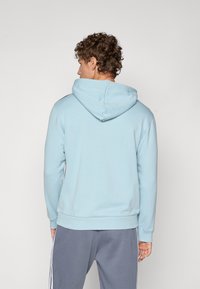 Light blue hooded sweatshirt with a kangaroo pocket and ribbed cuffs, paired with gray sweatpants featuring side stripes.