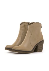 Botines beige de cuero liso, con una línea superior curva, cremallera lateral y un tacón de madera apilada con ranuras diagonales.