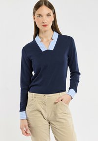 Marineblauw overhemd met lange mouwen en een V-hals, voorzien van een lichtblauwe gestreepte kraag en manchetten, gecombineerd met beige broeken. Soepele stof en stijlvolle pasvorm.