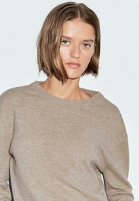 Maglione beige lavorato a maglia con scollatura rotonda e spalle scese. Texture morbida, peso medio, design minimalista, adatto per sovrapposizioni.