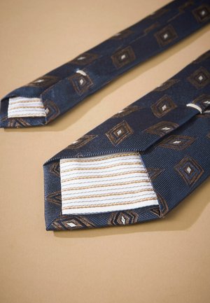 Mørkeblå slips med diamantmønster i brune og hvide accenter. Har struktureret stof med spids ende og stribet indvendig foring.