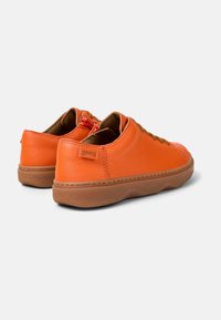 Zapatillas de cuero naranja con suela de goma marrón, con cordones redondos y una pequeña etiqueta de la marca en el talón. Material texturizado en toda su extensión.
