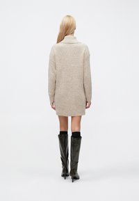 Rochie pulover bej tricotată, cu guler înalt, mâneci lungi și textură reiată, asortată cu cizme negre până la genunchi.