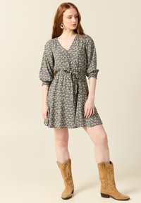 Blommönstrad klänning med V-ringning, inringad midja och puffärmar, matchad med beige mockakängor. Lätt, texturerad väv.