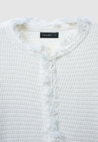 Cardigan bianco textured con scollo frangiato, caratterizzato da una chiusura senza bottoni e un'etichetta del marchio "CALLIOPE". Tessuto morbido e motivo intrecciato.