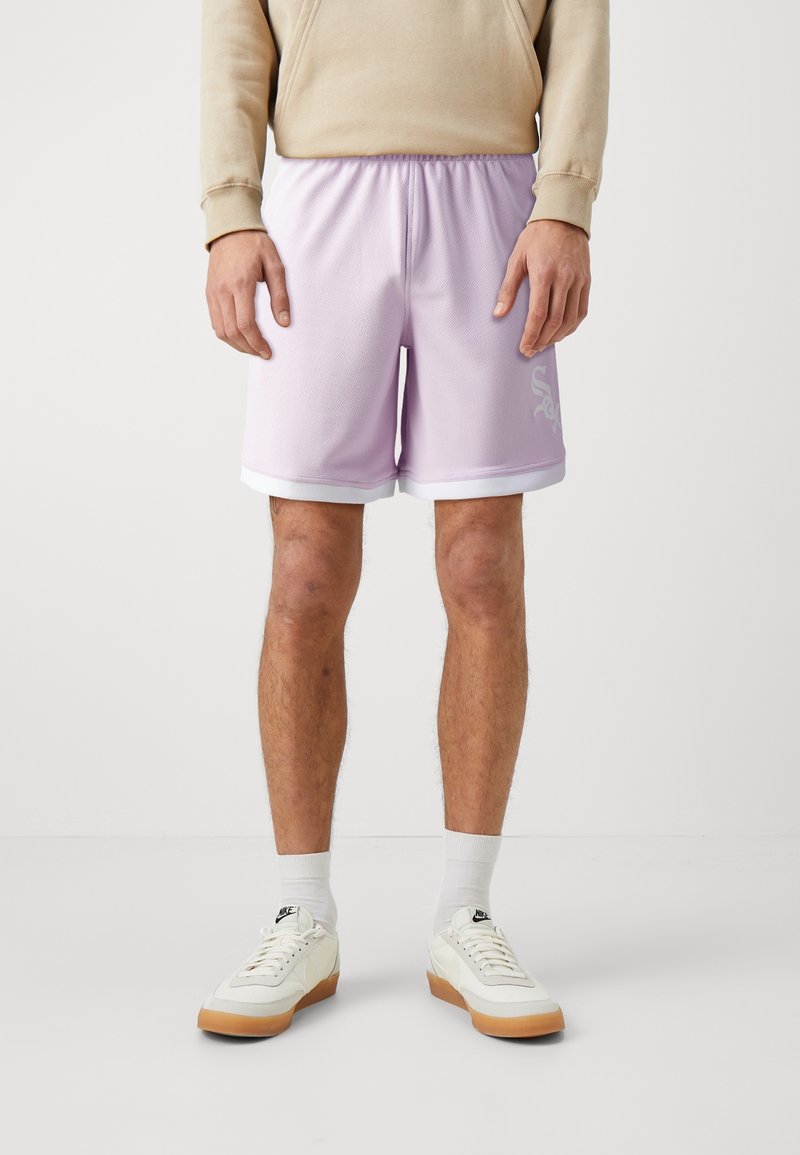 Shorts de sport en maille violette avec bordure blanche et logo sur le côté, dotés d'une taille élastique. Stylisés avec des baskets crème et des chaussettes blanches.