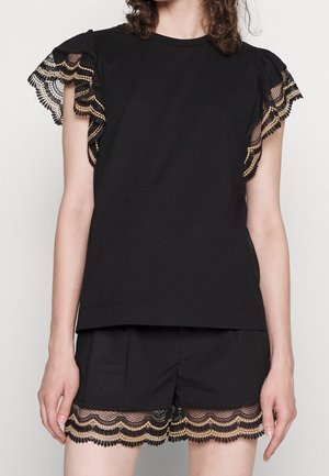 Femme portant un ensemble noir composé d'un haut et d'un short, avec un bord en dentelle noire et beige festonnée sur les manches et l'ourlet du short.