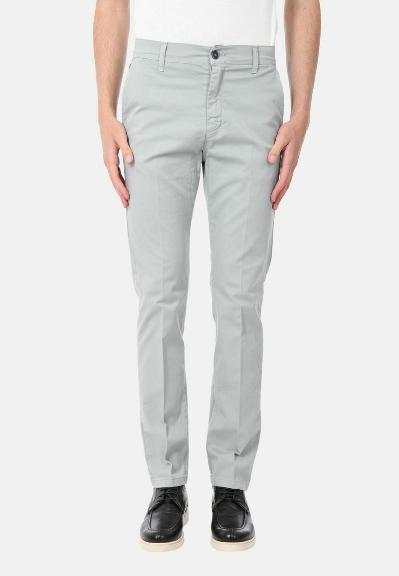 Pantaloni grigi chiari con vestibilità slim, realizzati in morbido cotone. Presentano una chiusura anteriore con bottone e tasche laterali. Indossati con scarpe nere.