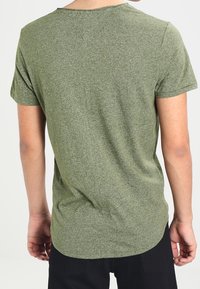 T-shirt verde oliva con maniche corte, scollatura rotonda, orlo leggermente curvato e tessuto testurizzato. Design semplice e casual.