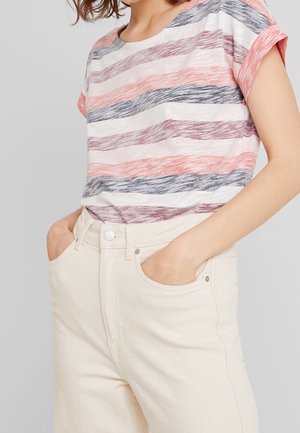 Femme portant un haut à manches courtes rayé multicolore, rentré dans un pantalon crème taille haute, les mains dans les poches.