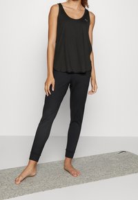 Top senza maniche nero con una vestibilità ampia e scollatura rotonda, abbinato a pantaloni sportivi neri aderenti con caviglie elastiche.