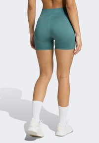 Shorts de sport turquoise avec une taille haute, texture lisse et motif rayé subtil. Associés à des chaussettes blanches et des sneakers.