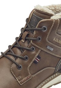 Bottines en cuir marron avec doublure en textile, présentant un design à lacets, des œillets en métal et des coutures contrastantes. Patch logo et accents de couleur inclus.