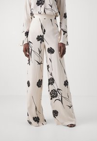 Crème wijdvallende broek gemaakt van soepele stof, met een zwart bloemenpatroon. Hoge taille met een relaxte pasvorm en vloeiende silhouet.