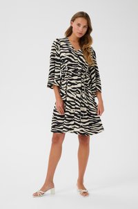 Robe rayée noir et blanc avec un design enveloppant, taille élastique et manches trois-quarts. Portée avec des sandales à talons blanches.