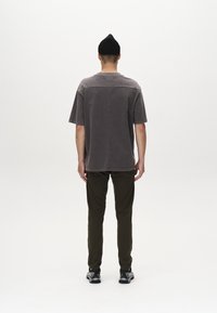 Una camiseta gris de gran tamaño con mangas cortas y un escote plano, combinada con pantalones verde oliva y zapatillas deportivas negras. Tejido liso y texturizado.
