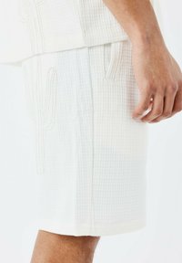Witte textuur shorts met een wafelpatroon, voorzien van een geborduurd cactusdetail en zijzakken. Lichtgewicht stof, ruime pasvorm.