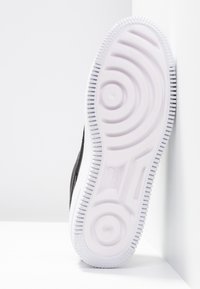 Svart sneaker med en vit gummisula. Har böjda fåror och cirkulära accenter på yttersulan. Överdelen har en texturerad yta.