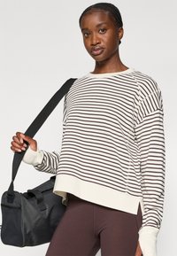 Gestreifter Langarm-Sweatshirt in Creme und Braun mit gerippter Textur. Verfügt über eine lockere Passform, fallende Schulternähte und eine verkürzte Länge.