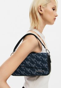 Borsa a spalla blu navy con esterno in tessuto a motivo, dettagli in pelle nera e logo argentato. Presenta una forma curva e una tracolla regolabile.