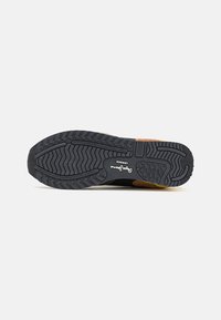 Semelle en caoutchouc noir avec motif de traction texturé et accents en suède marron. Présente un logo imprimé au bas. Conçu pour un usage athlétique et décontracté.