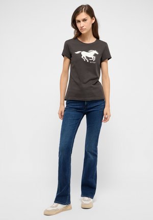 Dark gray cotton t-shirt featuring a white horse graphic. Paired with blue flared jeans and beige sneakers with textured accents.