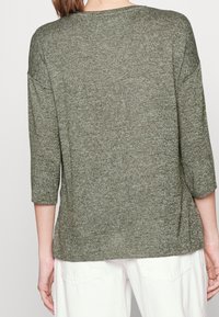 Pull vert olive avec un tricot texturé, manches trois-quarts et coupe décontractée, coutures visibles et encolure arrondie.