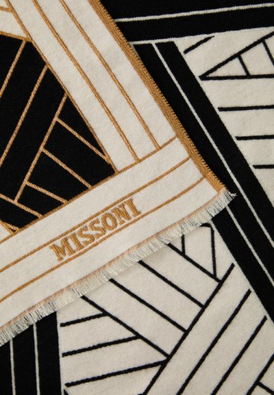 Juodas ir kremas pledas su geometriniais raštais. Savybė – auksinis logotipas ir kutai, pagamintas iš minkštos tekstūrizuotos medžiagos.