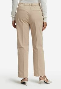 Beige midjebyxor med bakfickor, rak benpassform och lätt glans; bärs med ljusa klackskor.