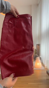 Piros műbőr szoknya sima felülettel, közepes hosszúságú, oldalán egy apró zsebbel ellátott derékkal és diszkrét fényes hatással.