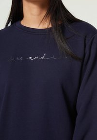 Mörkblå sweatshirt med rund halsringning. Har silverreflekterande text som säger "live and die" över bröstet. Tillverkad av bomull, avslappnad passform.