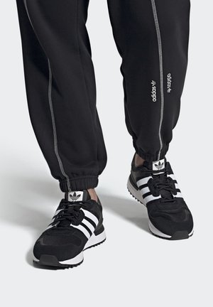 Zapatillas deportivas negras con rayas y acentos blancos, que cuentan con una parte superior de malla transpirable, suela de goma y un diseño acolchado. Pantalones de jogging ligeros.