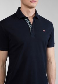 Polo shirt blu navy con tessuto testurizzato, caratterizzato da un colletto con motivo e un piccolo logo a forma di bandierina rossa sul petto sinistro.