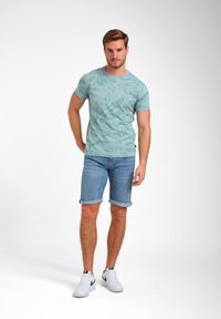 Šviesiai mėlyna trumpomis rankovėmis marškinėliai su lapų raštu, derinami su sukritusiais džinsiniais šortais. Baltos sportinės bateliai užbaigia kasdienį įvaizdį.