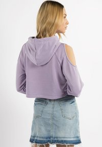 Felpa corta viola con cappuccio, caratterizzata da aperture all'altezza delle spalle. Indossata con una mini gonna in denim chiaro con orlo sfrangiato.