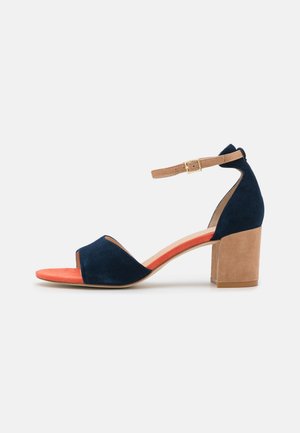 Marineblå ruskind sandal med åben tå, kontrasterende orange indersål, robust beige blokhæl og justerbar ankrem med gulddetaljer.