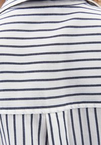 Tessuto bianco con righe orizzontali blu navy sopra una cucitura, che si trasforma in righe verticali blu navy sotto la cucitura.