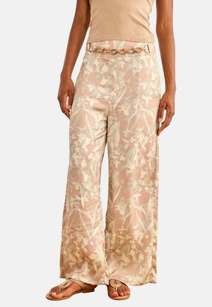 Mujer con pantalones beige de pierna ancha con estampado floral y cinturón de cadena dorada, combinados con top y sandalias marrón claro.