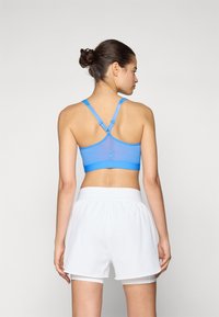 Top curto atlético azul com um design em rede, alças ajustáveis e fundo elástico, combinado com calções atléticos brancos.