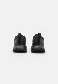 Black athletic shoes featuring a textured fabric upper, padded collar, and a rugged rubber sole with deep treads. Vertical pull tab at the heel.